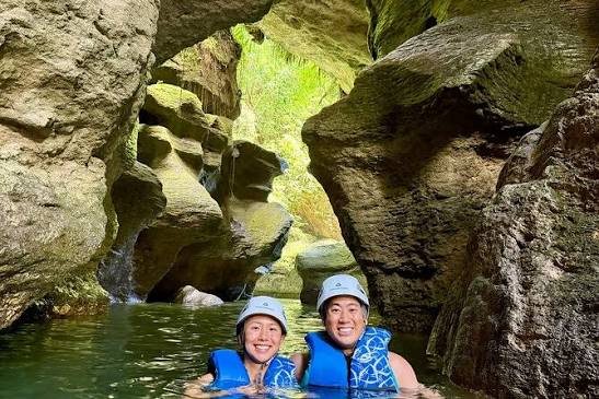 Dos personas sonrientes con chalecos salvavidas dentro del agua de una cueva