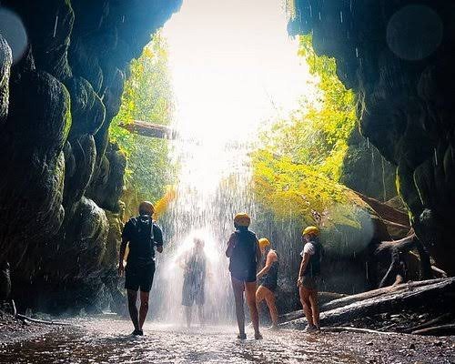 Caminantes avanzando por una cueva hacia una cascada iluminada por el sol