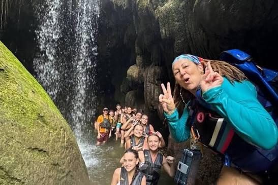 Grupo grande de caminantes sonriendo bajo una cascada dentro de una cueva
