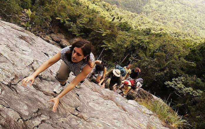 Personas subiendo una roca en un sendero de montaña, ayudándose entre sí